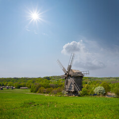 Naklejka na ściany i meble wooden authentic windmill among green fields at the sunny day, historical farm scene