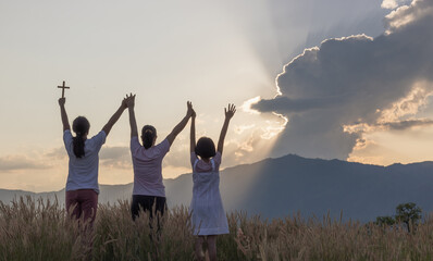 Silhouette of happy family praying and holding christian cross for worshipping God at sunset...