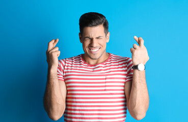 Man with crossed fingers on light blue background. Superstition concept