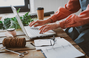 Fashionable stylish girl hipster florist in a work apron working at a laptop, looking at a...