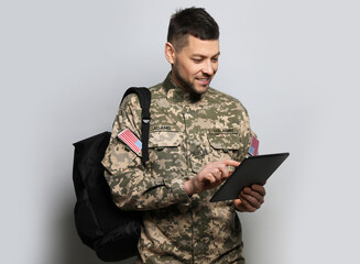 Cadet with backpack and tablet on light grey background. Military education