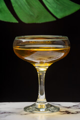 Close-up of glass of whiskey sour, on white marble table, selective focus, black background with green leaf, vertical