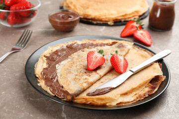 Delicious thin pancakes with chocolate paste and strawberries on grey marble table