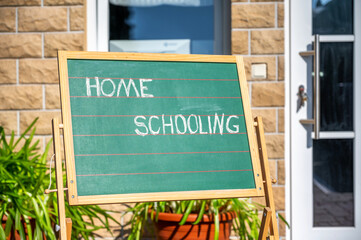 Kreidetafel mit dem Wort Homeschooling im Garten eines Wohnhauses