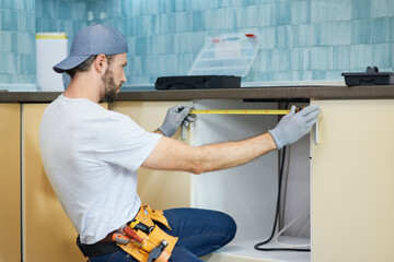 Young repairman, professional plumber using measure tape while doing plumbing work in a new flat...