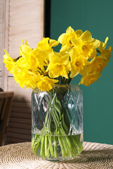 Beautiful daffodils in vase on wicker table indoors