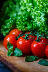 Close-up photo of advertising tomatoes and greens with drops of dew.