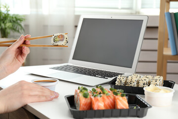 Woman having tasty sushi rolls for lunch at workplace, closeup