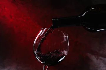 Fotobehang Gieten van rode wijn uit fles in glas op kleur achtergrond, close-up © New Africa