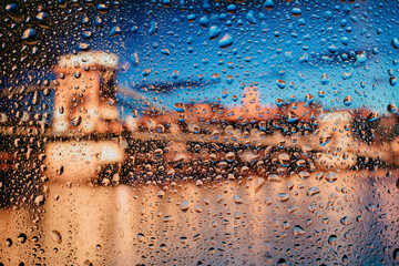 Beautiful landscape conceptual view of the city through glass window with raindrops. Rain at urban night view of the city.