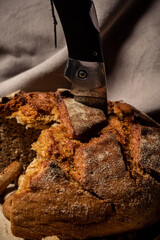 Knife stuck in bread on a wooden stand on a brown background