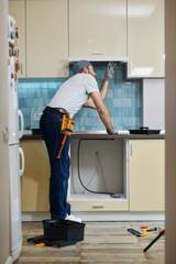 Fix anything. Full length shot of young handyman examining a kitchen extractor before fixing it,...