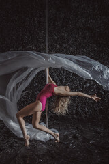 Obraz na płótnie Canvas Blonde sportswoman in a beautiful sports pink leotard on a pole doing beautiful elements dancing