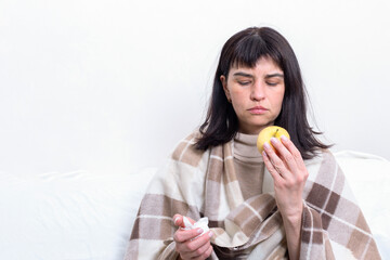 Portrait of a sick attractive woman wrapped in a blanket holding an apple. The girl is at home in quarantine