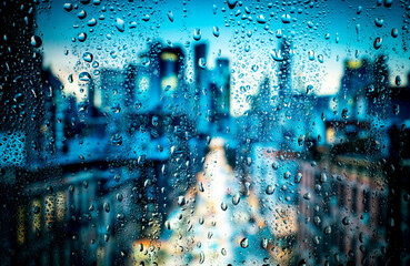 Beautiful landscape conceptual view of the city through glass window with raindrops. Rain at urban night view of the city.