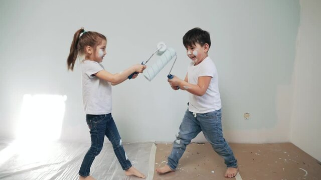 Caucasian boy and girl paint the wall with rollers Brother and sister paint on the wall with paint Children get dirty in paint and have fun Children make repairs in the room Happy family