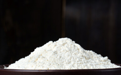Heap of wheat flour in a plate on a wooden black background with copy space. banner