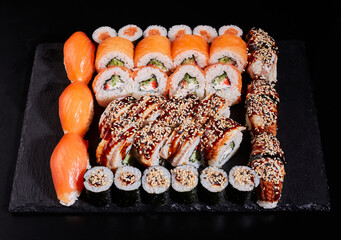 Different types of appetizing rolls on a stone plate on a black background.