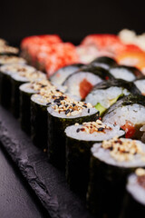 Close up of little maki sushi sprinkled with sesame seeds in a row on a slate of black stone.