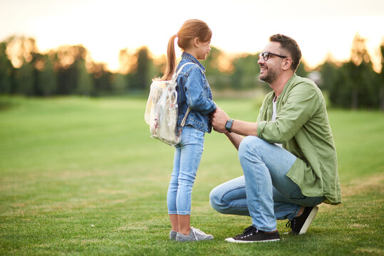 Side View Of Joyful Young Father Smiling While Holding Daughter's Hands, Daddy Spending Time With His Little Girl In The Green Park On A Warm Day