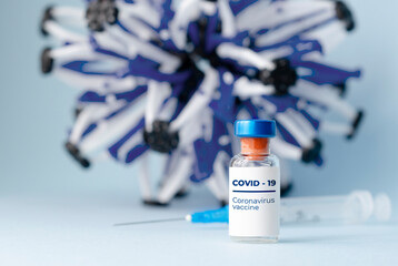 Ampoules in hand and syringe with Covid-19 vaccine on blue background. For the prevention, immunization and treatment of coronavirus infection.Infectious medicine concept. With copy space