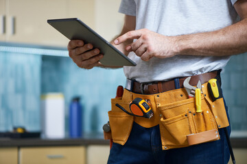 Cropped shot of young repairman wearing a tool belt with various tools using digital tablet while...