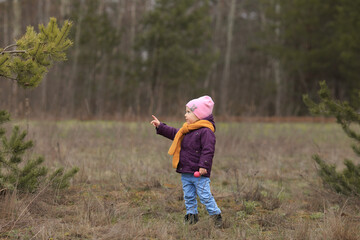 a small child stands and points to a green branch
