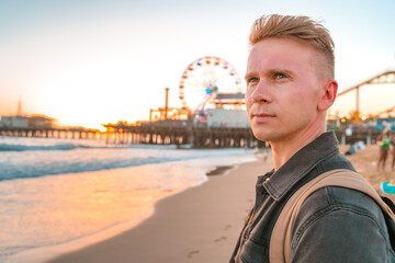 Young blonde man on Santa Monica beach against the background of an orange sunset in Los Angeles,...