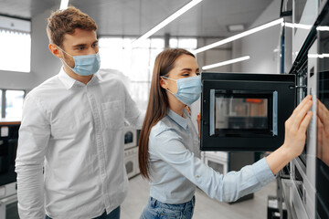 Fototapeta na wymiar Young couple wearing medical masks in hypermarket with home appliances