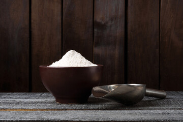 a plate of wheat flour and a scoop on a dark background with copy space. banner