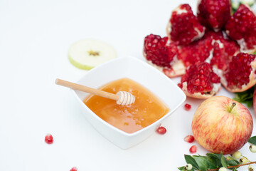 Creative layout of traditional symbols for jewish holiday - pomegranate, cup with honey, apple and green branch on white background. Concept Rosh Hashanah tova jewish New Year. Side view, fresh fruits