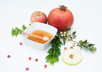 Creative layout of traditional symbols for jewish holiday- cup with honey, apple, pomegranate, green branch on white background. Concept Rosh Hashanah tova jewish New Year. Side view, fresh fruits