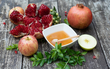 Creative layout of traditional symbols for jewish holiday - apples, cup with honey, pomegranate, green branch on wooden background. Concept Rosh Hashanah tova jewish New Year. Top view, fresh fruits