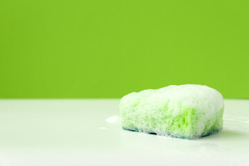 Green kitchen cleaning sponge with soap bubbles lying on white background. Front view