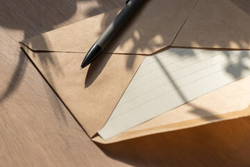 Lined sheet of paper in craft envelope and pencil lie on the table. Still life in rays of the...