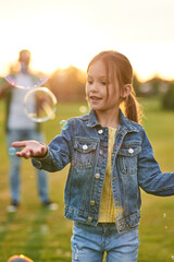 Lovely little girl having fun with soap bubbles on a sunny day, daughter and dad spending time...
