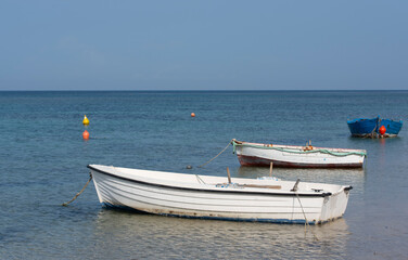 Naklejka na ściany i meble On the coast of the Mediterranean there are three small, empty, old fishing boats under a blue sky