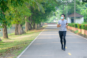 Fototapeta na wymiar Young asian man Wear a fitness mask Run in the park Sweating from a morning workout concept: wear a mask against SARS-Cov-2.