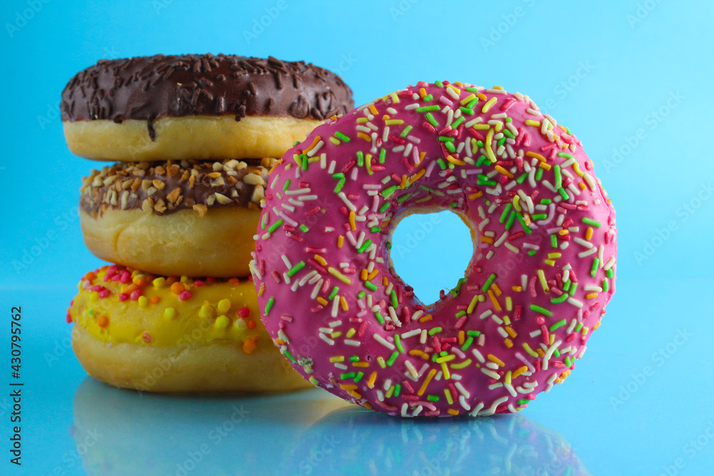 Wall mural A still life eating sweet donut berliners in a pink glaze with a colored sprinkler stands next to a stack of doughnuts on a blue bright background with a place to text a picture for the table