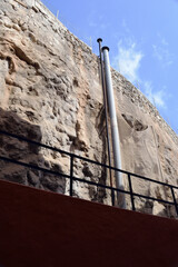 Industrial Steel Chimney on Face of Steep Cliff behind Commercial Buildings with Handrail & Blue...