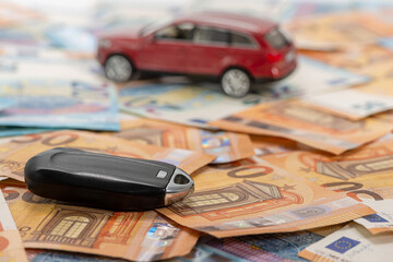 key and red toy car on pile of euro banknotes, buy or sell a car, rent a car or insurance concept