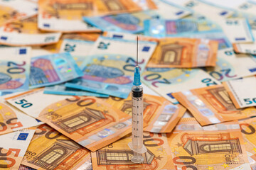 spread stack of Euro banknotes with syringe on top of them, health costs concept