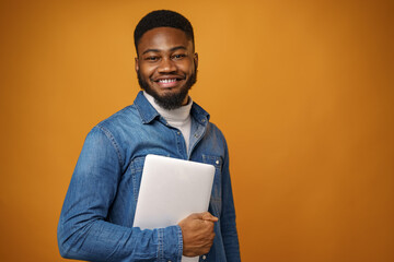 Young african american man standing with laptop against yellow background