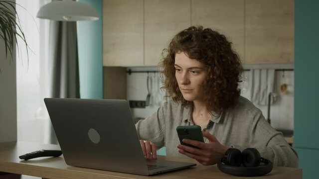 Young 20s woman browsing on her smart phone and double checking on her laptop while shopping online