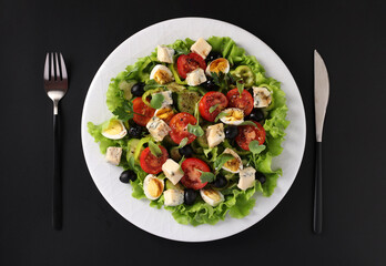 Healthy salad of cherry tomatoes, cucumbers, peppers, black olives, quail eggs and gorgonzolla cheese on black background, top view