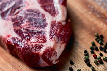 raw pork steak with lard layers is ready for cooking, lies on a wood board with garlic, rosemary, salt and peppercorns. future meat delicious, side view