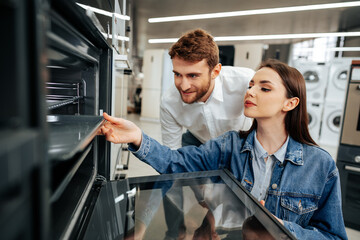 Young couple choosing new electric oven in hypermarket