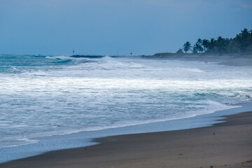 Two people walking in the distance as a ray of sunlight shines on the water's edge at Blowing Rocks in Florida.
