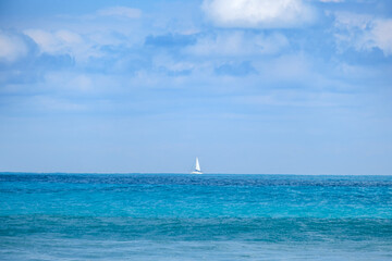 Fototapeta premium A lone white sailboat sits on the vast blue horizon in the Atlantic Ocean.