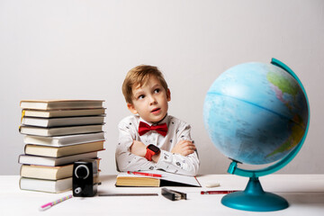 A little boy in a white shirt and a red bow tie with a big car smart watch on his hand does his homework for school.